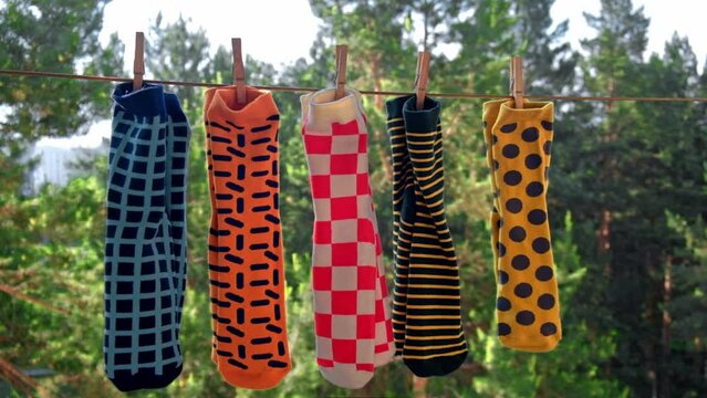colorful bright men's socks with different patterns are dried on the balcony on a rope in pairs, attached with wooden clothespins. against the background of the trees. close-up. slow motion.