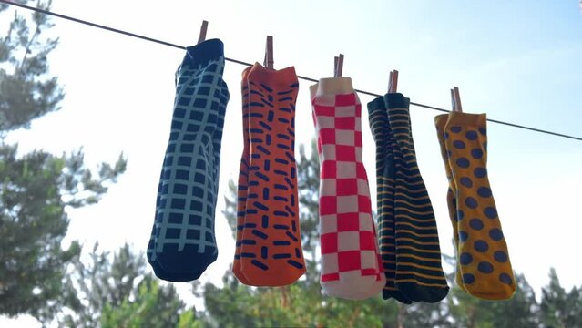 fashionable multi-colored men's socks with different patterns are dried on balcony on rope in pairs, attached with wooden clothespins. against the background of sky and trees. close-up. slow motion.