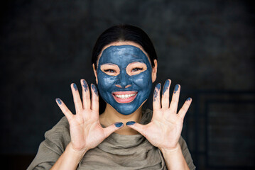 shot of young attractive woman with white towel on her head, has naked body, smilling isolated over pink background in studio, looks aside, having chocolate mask on her face. Skincare concept