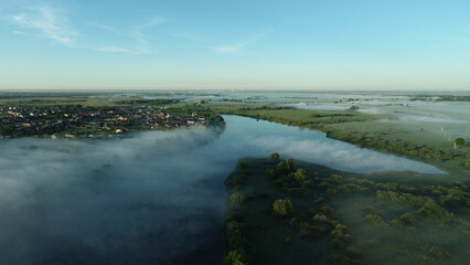 Bird's eye view of the mist over the river and meadows on an early summer morning