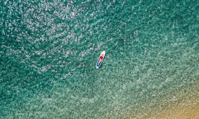Aerial view of woman  lies down on a paddle board and enjoys relaxation on tropical sea