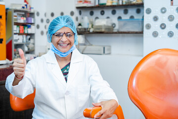Happy smiling woman dentist showing thumbs up gesture by looking camera at dental clinic - concept of successful, healthcare service and hygienist.
