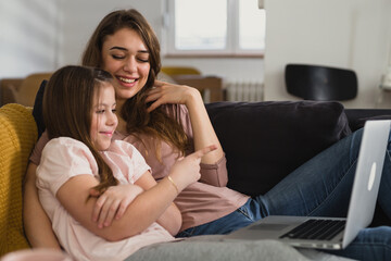 mother and daughter laying on sofa in living room and using laptop computer
