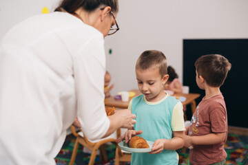 teacher gives breakfast to kids in kindergarden