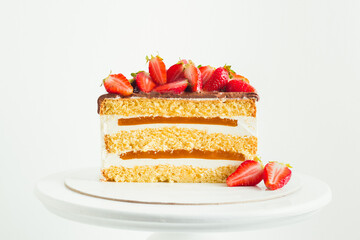 Summer cake decorated with strawberries on the white background. Yellow sponge bisquit cake cut with cream cheese and berry mousse layers
