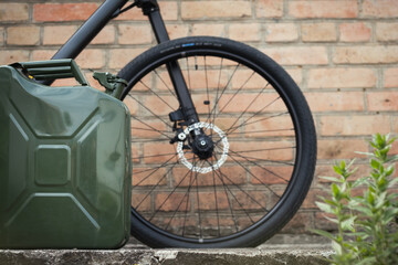 Green Jerrycan against red brick wall. Empty Gas canister next to the bicycle. Cycling while fuel shortage