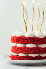 Birthday cake with red velvet sponge layers and white cream cheese filling decorated with lit golden candles