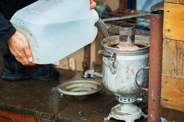 Pouring drinking water from a canister into an old samovar on the steps of a wooden house. Rainy...
