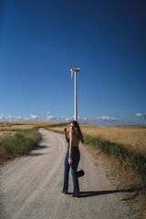 Chica joven delgada con pelo ondulado posando en camino de tierra con molinos de viento  de fondo