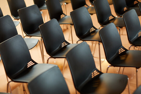 Background image of empty black plastic chairs in rows standing in auditorium for seminar and training class