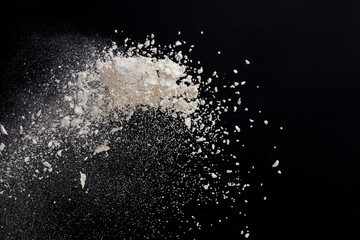 Flying white flour, powder on a black background. Spray of particles, lumps, pieces of white...