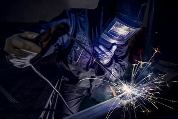 Arc welding. The welder works with an electric welding machine. Sparks of red-hot metal scatter in...