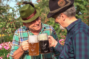Senior men with beer mugs with Bavarian beer in Tyrolean hats celebrating a beer festival in Germany. Happy old people during the October holiday in Munich