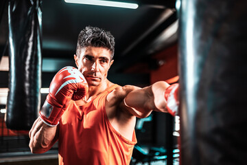 Handsome middle aged man boxer is exercising with a punching bag at training fitness gym.male boxing workout sport.
