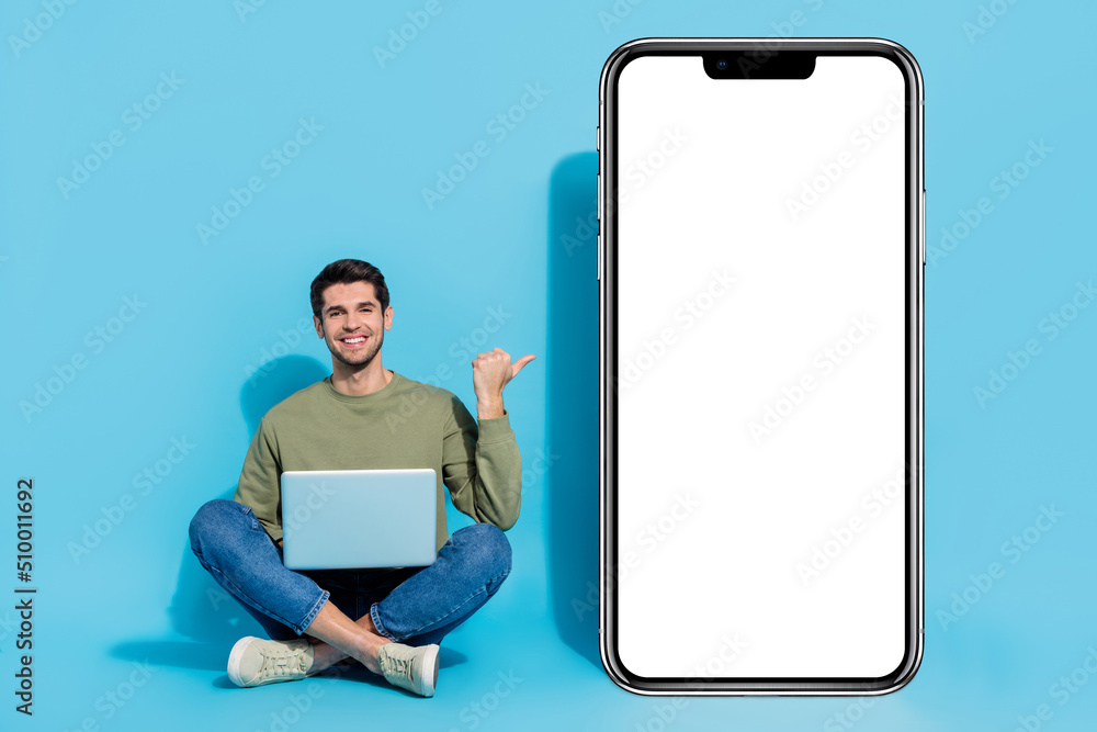 Poster full size portrait of cheerful man sit floor direct thumb empty space huge phone isolated on blue co