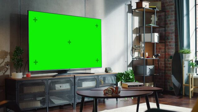 Big Green Screen Television on Modern Console in Simple Loft Living Room. Green Chroma Key TV in the Middle of the Room. Zoom On Camera Shot