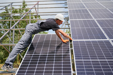 Man engineer solar installer placing solar module on metal rails. Male worker installing...