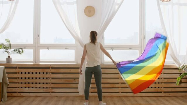 Female holding LGBT gay flag in hands and waving on sunset in sunny rays. Rainbow LGBT flag - Lesbian, gay, bisexual, transgender social movements. High quality 4k footage