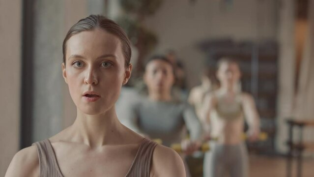 Chest up slowmo of young Caucasian woman doing dumbbell front raise during group workout in pilates studio