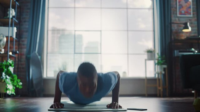 Athletic Black Man Doing Push Up Exercises, while Using Mobile Smartphone as Timer. Authentic Male Doing Workout, He is Training at Home with Minimalistic Interior. Establishing Shot