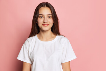 Fototapeta premium Half-length portrait of young pretty girl in white t-shirt isolated on pink background. Concept of beauty, art, fashion, youth and emotions