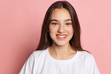 Fototapeta premium Half-length portrait of young pretty girl in white t-shirt isolated on pink background. Concept of beauty, art, fashion, youth and emotions