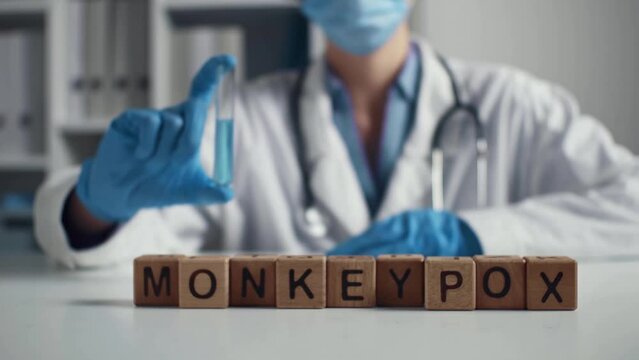 Doctor in a protective mask, a collage on the theme of the monkeypox pandemic. Inscription from wooden cubes of monkeypox and a doctor with a test tube. The study and prevention of smallpox. 