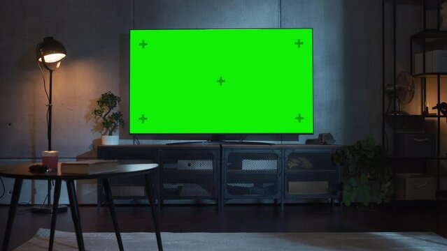 Stylish Loft Apartment Interior with TV Set with Green Screen Mock Up Display Standing on Television Stand. Empty Living Room at Home with Chroma Key Placeholder on Monitor. Zoom On Shot