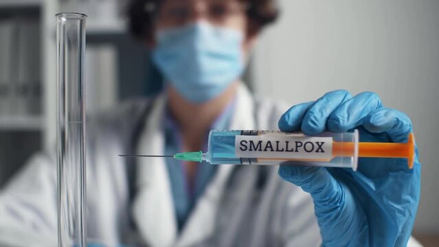Syringe smallpox vaccine syringe doctor's blurred face. Mandatory vaccination during dangerous epidemic of influenza smallpox. Doctor holds syringe with vaccine. A new virus is spreading in a pandemic