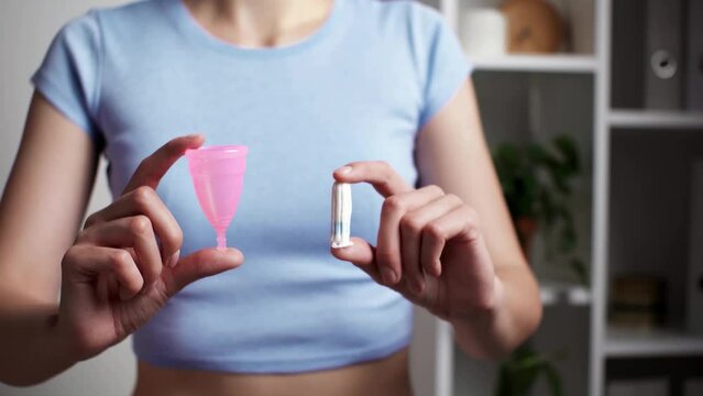 Young woman without a face holds in her hands various types of feminine hygiene products - a menstrual cup and a tampon. Choosing between a tampon and a menstrual cup. Eco friendly zero waste concept
