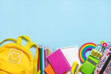 Back to school, education concept Yellow backpack with school supplies - notebook, pens, eraser rainbow, numbers isolated on blue background Top view Copy space Flat lay composition