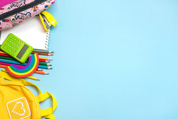 Back to school, education concept Yellow backpack with school supplies - notebook, pens, eraser rainbow, numbers isolated on blue background Top view Copy space Flat lay composition