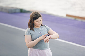 Overweight European teenage girl in tracksuit watches time and distance on smart fitness bracelet...