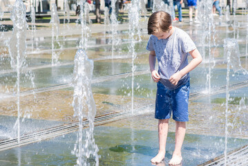 happy child plays in a dry fountain. joyful smiling boy stands wet in the fountain