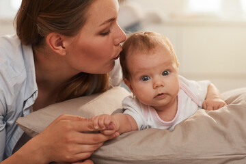 Pretty young mother kissing her curious adorable little baby crawling on bed
