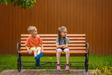 Boy and girl sitting on a bench. On a sunny summer day, a five-year-old boy and a girl are sitting on a bench in the garden.