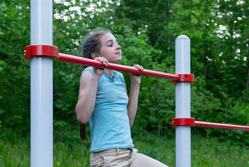 Fototapeta na wymiar Sportive teenage girl is making pull ups on the horizontal bar outdoors 