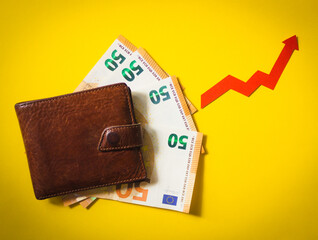 Wallet above the euros and the red arrow on the yellow surface. Financial background. Concept of investment, rising cost of living and inflation.