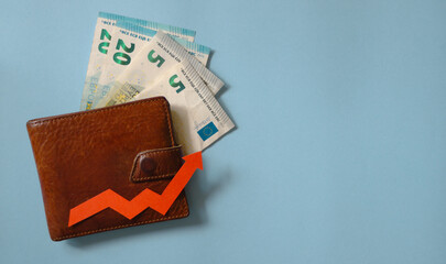 Wallet above the euros and the red arrow on the light blue background. Concept of financial growth, rising cost of living and currency exchange