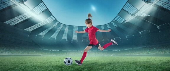 Portrait of little girl, football player in red uniform in motion, hitting ball at the open air stadium. Championship