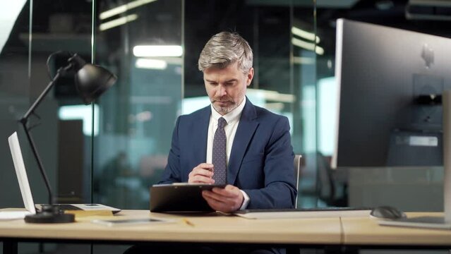 Senior business man signs a approval document in the office. Mature gray successful banker or lawyer businessman reading and signing business partnership contract. employee doing paper work