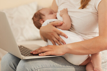 Young mother feeding baby with breast milk and working on computer on her laps