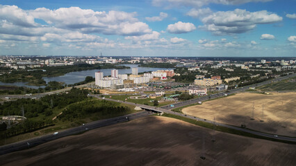 Obraz premium Agricultural fields on the outskirts of the city. You can see the city blocks. New sprouts of agricultural crops appear on the field. Blue sky with clouds. Flight in the suburbs. Aerial photography.
