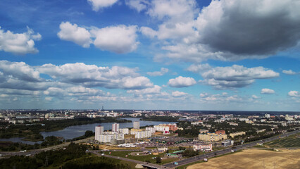 Fototapeta premium Agricultural fields on the outskirts of the city. You can see the city blocks. New sprouts of agricultural crops appear on the field. Blue sky with clouds. Flight in the suburbs. Aerial photography.