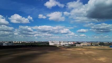 Naklejka premium Agricultural fields on the outskirts of the city. You can see the city blocks. New sprouts of agricultural crops appear on the field. Blue sky with clouds. Flight in the suburbs. Aerial photography.