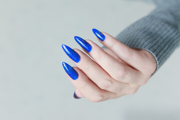 Female hand with long nails and a bottle of light blue color nail polish