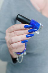 Female hand with long nails and a bottle of light blue color nail polish