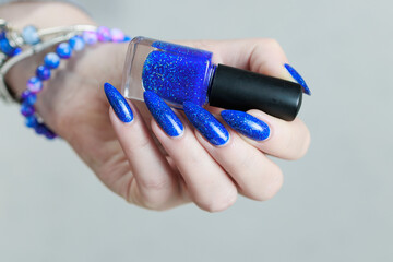 Female hand with long nails and a bottle of light blue color nail polish