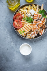 Plate with grilled haloumi, souvlaki, greek-style fries with feta and tomatoes. Flat lay on a grey concrete background, vertical shot with space