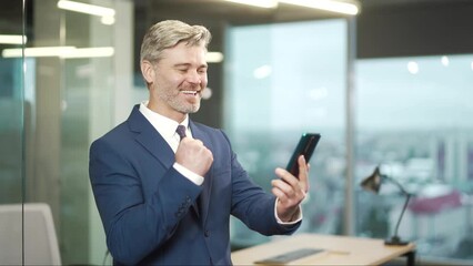 Excited mature business man hold smartphone overjoyed businessman ceo executive winner celebrate mobile online bid game win victory success receive read good news on cellphone expression at office